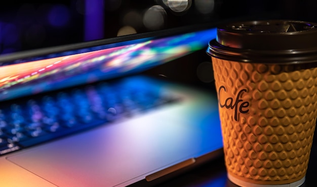 Photo a laptop half closed in the dark with colourful glow and cup of coffee