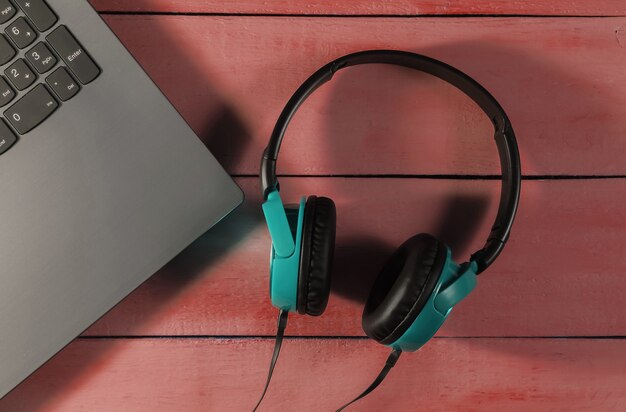 Laptop and headphones on red wooden background. Top view. DJ equipment