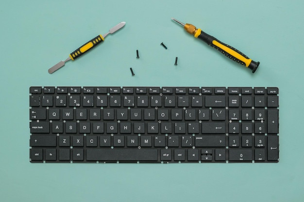 Laptop keyboard and screwdrivers with screws on a blue background