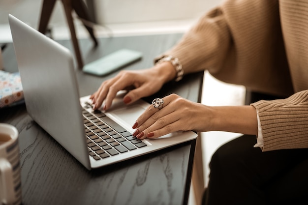 Laptop keyboard. Tidy woman in beige sweater with red manicure and having rarity ring on her point finger