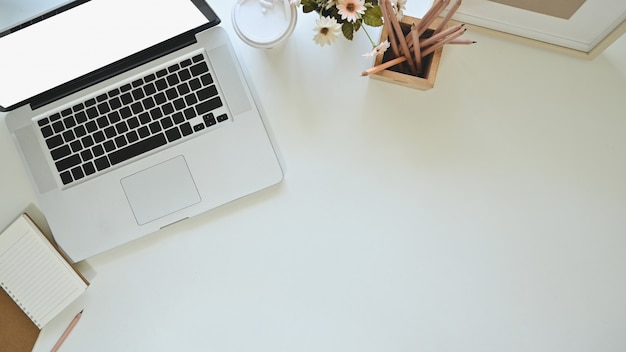 Laptop, koffie, notitieboekjedocument en potlood van het bureaubovenkant met fotokader en bloem op exemplaarruimte.