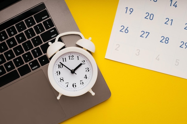 Laptop maandelijkse kalender en wekker op gele achtergrond Deadline concept