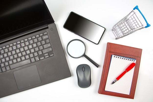 Ноутбук увеличительное стекло компьютерная мышь смартфон ручка блокнот на белом фоне Товары для бизнеса и покупки товаров в Интернете