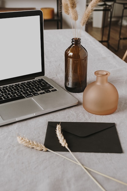 Foto laptop met blanco display, envelop, pluizige planten, rogge / tarwe-oorstengels, decoraties op grijs gewassen linnen doek