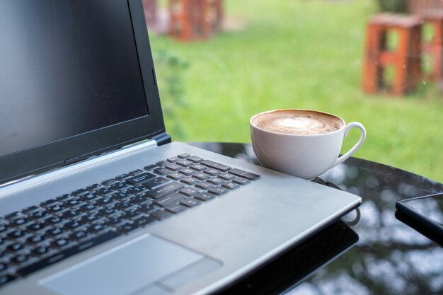 Laptop met latte warme koffie in witte kop op glazen tafel