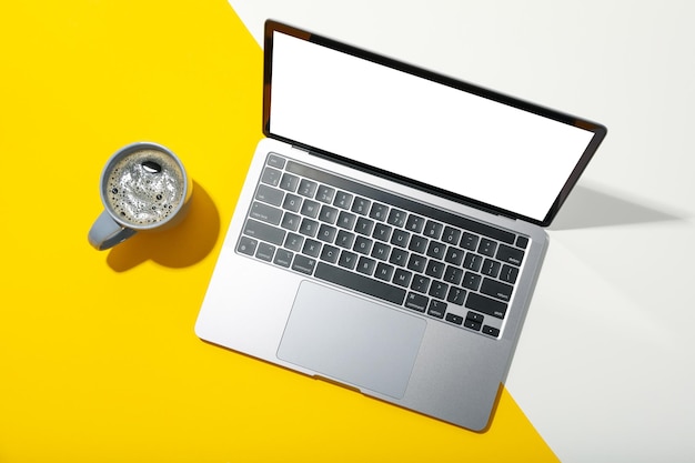 Laptop met leeg scherm en kopje koffie op tweekleurige achtergrond