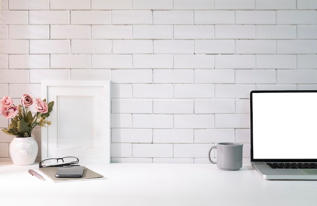 Laptop met leeg scherm fotolijst bloempot en notitieboekje op witte tafel vrouwelijke werkplek