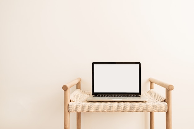 Laptop met leeg scherm op rieten bank tegen witte muur.