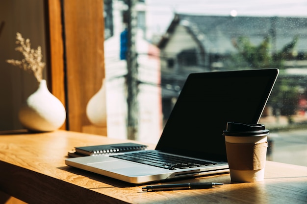 Laptop met papieren koffiemokken, pen op tafel.