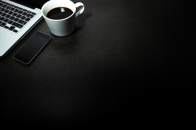 Laptop, Mobile phone and a cup of black coffee against empty dark background, working office theme