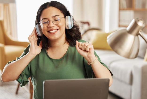 Laptop music and headphones with a woman in her home listening to the radio in the living room to relax Computer audio and streaming with a young female student in her house for education