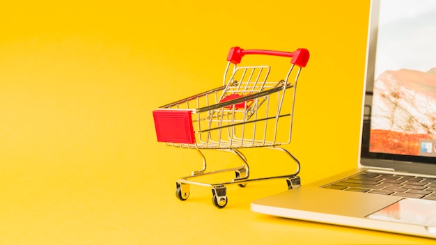 Foto computer portatile vicino al carrello del supermercato con manico rosso