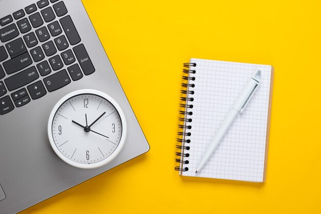 Laptop, notebook and alarm clock on yellow background. Time running away. The concept of urgent deadlines at work and commitments.