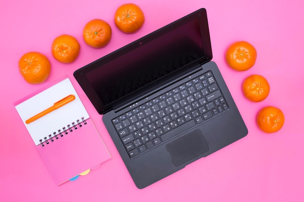 Laptop notebook pen en mandarijnen op een roze achtergrond