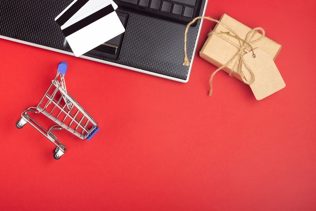 Фото Ноутбук, ноутбук, корзина и коробки на ярко-красном фоне. концепция покупок в интернете