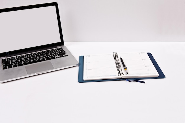 A laptop and a notebook on a table with a pen on it