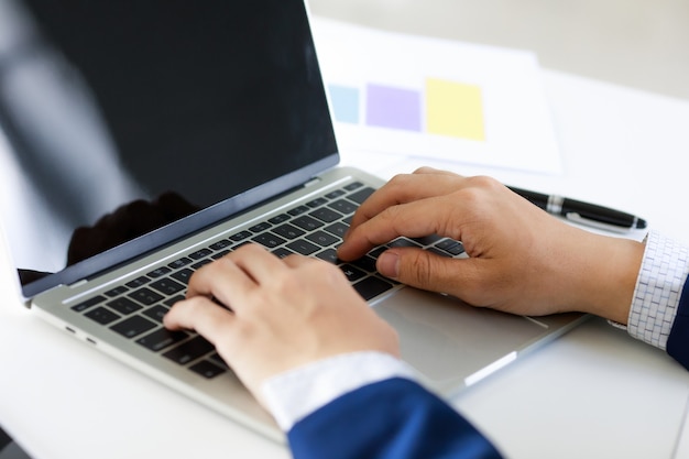 Laptop on office tablen with business man's hand in navy blue suit typing . Concept for cool style workplace.