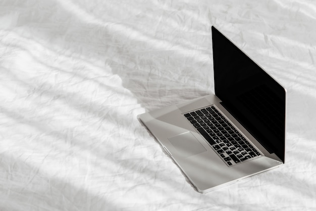 사진 흰색 침대에 있는 노트북은 가정 개념에서 작동합니다. 아침 빛