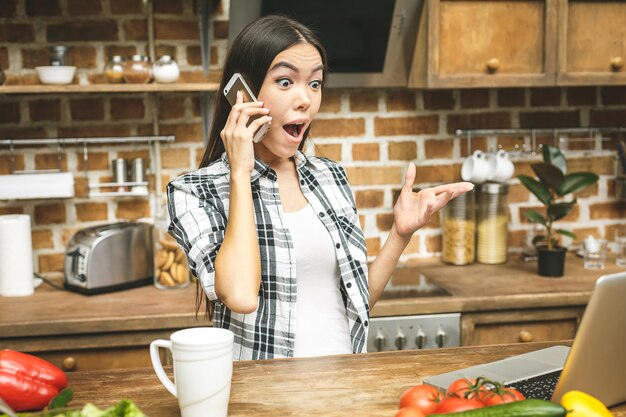 Laptop op de keukentafel en koken meisje. Verrast meisje