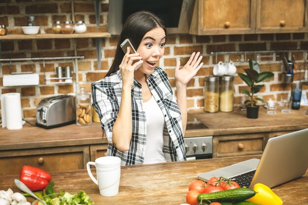 Laptop op de keukentafel en koken meisje. Verrast meisje