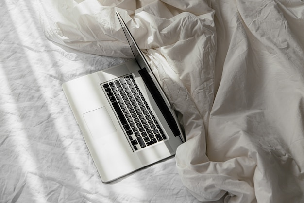 Laptop op wit bed met een deken. Werk thuis concept. Ochtend licht