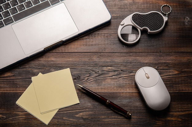 Laptop opened magnifier mouse pen and paper for taking notes on the dark wooden table close up