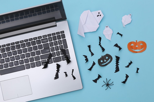 Laptop and paper-cut Halloween decor on blue background. Top view. Flat lay