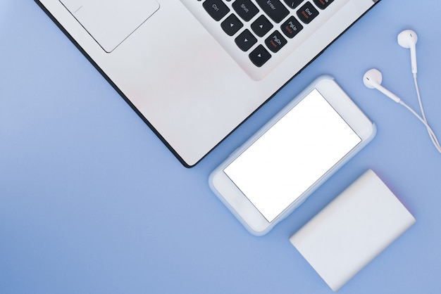 Laptop, phone, headphones and power bank on a blue background. Flat Lay composition and place for text. Top view.