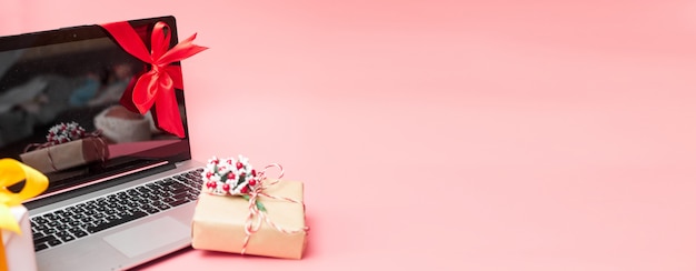 Photo laptop in a red ribbon with gifts, on a pink background, banner, copy space