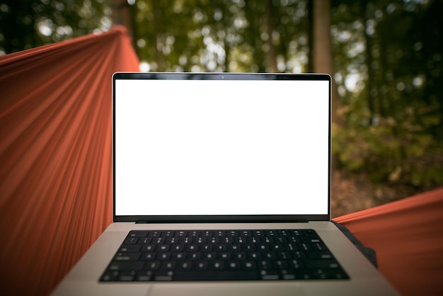 Laptop of a remote digital nomad on a hammock with green forest\
background first perspective working on a modern laptop while in\
nature