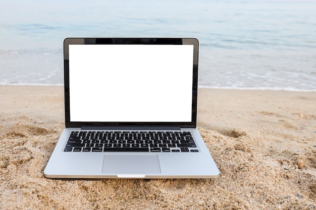 Ноутбук на песке на пляже летом в фоновом режиме с белым экраном.