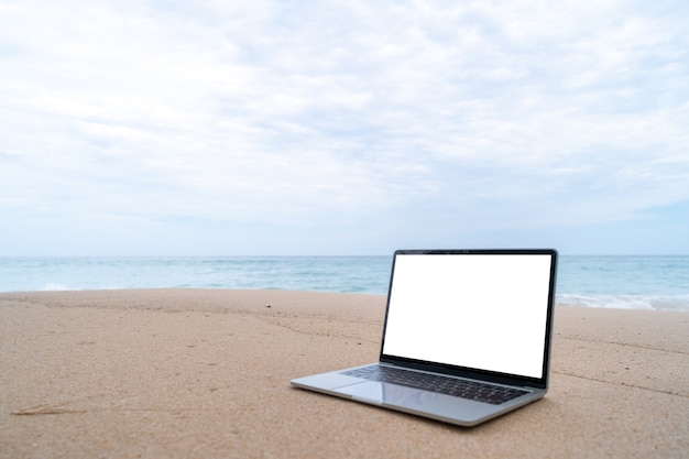 Laptop on sand at summer beach in background.