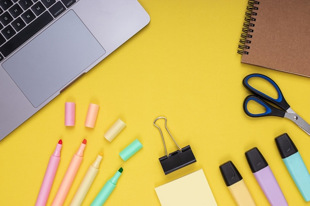 Laptop scissors clamp notepad colored pencils back to school Isolated yellow background