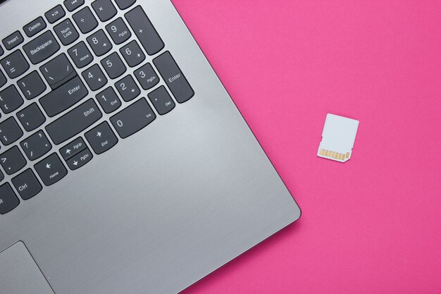 Laptop and SD memory card on pink paper with geometric shapes