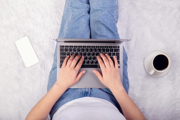 Laptop smartphone and coffee cup in girl's hands sitting on white blanket Flatlay freelance rest