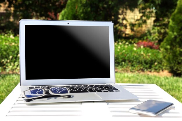 Photo laptop smartphone and glasses on wooden table outdoor