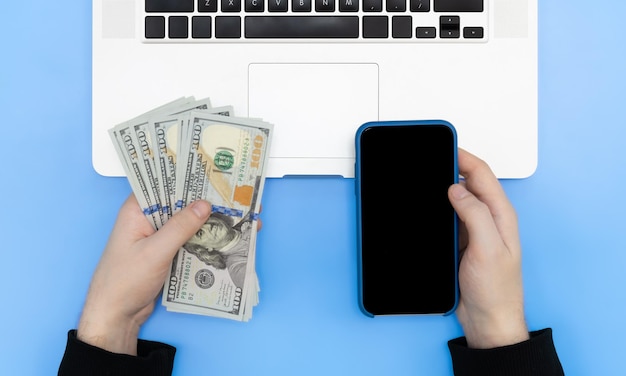 Photo laptop smartphone and money in male hands top view