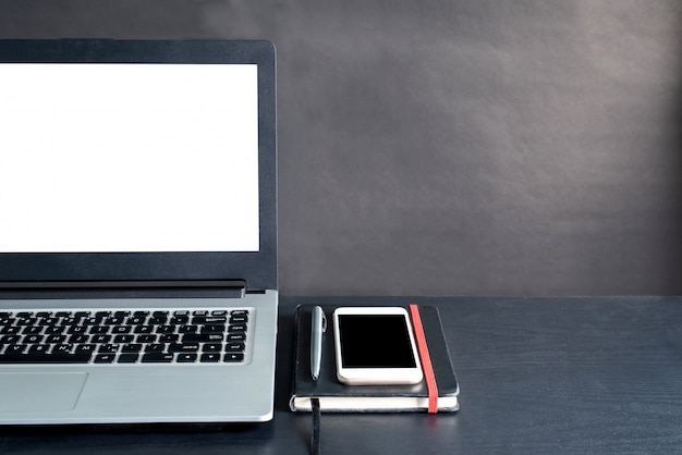 Laptop, smartphone, notebook, pen, on black wooden table with black background