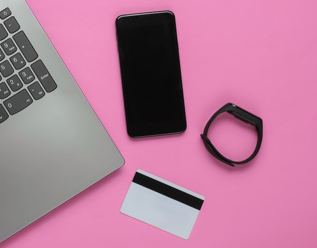 Laptop, smartphone, smart bracelet and bank card on pink background. Online shopping. Top view