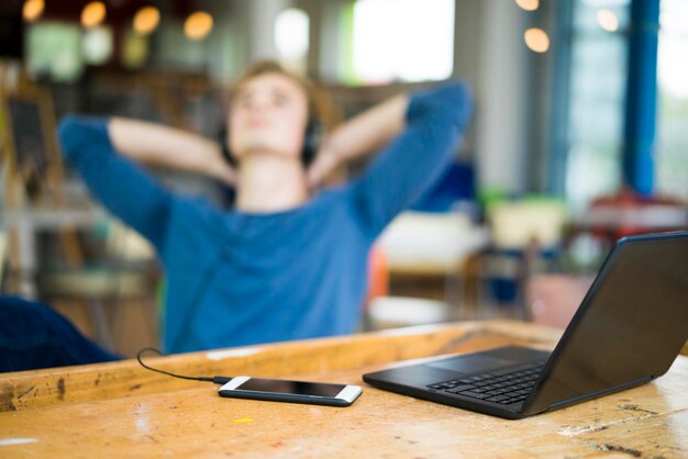 Laptop and smartphone on table with relaxing young man listening music in the background