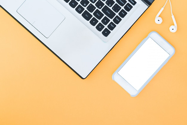 Laptop and smartphone with a white screen and headphones on the orange background.