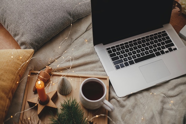 Photo laptop on soft bed cup of tea christmas lights stars pine candle pillows freelance and blog