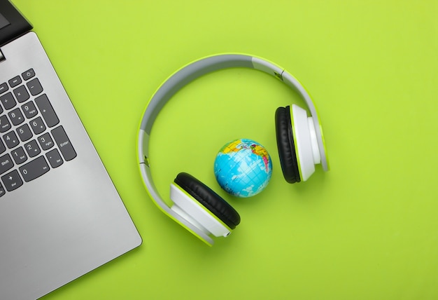 Laptop, stereo headphones and globe on green surface