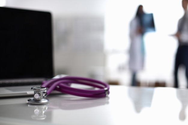 Laptop and stethoscope on the desk, doctors standing in the background