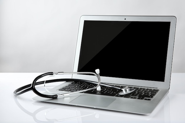 Laptop and stethoscope on white table