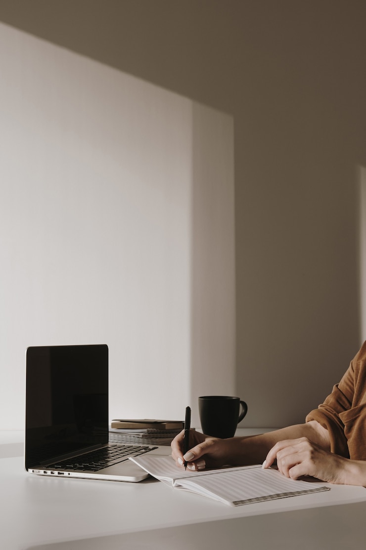Photo laptop on table with coffee cup, paper sheet, stationery against white wall