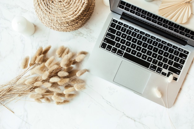 Laptop, tan plant branches bouquet on marble table