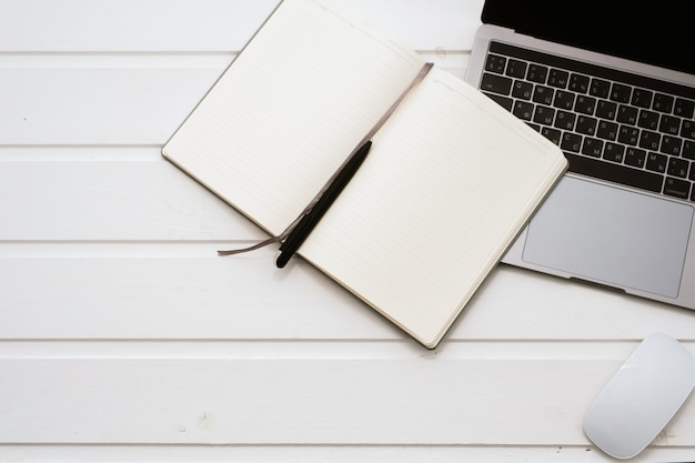 Laptop toetsenbord, muis en leeg notitieboekje op een witte houten achtergrond. Zakelijke thema sjabloon