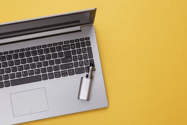 Laptop and vaping device on yellow background Flat lay