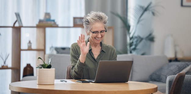 Laptop video call and remote work with a senior woman at work in her home office for business communication Computer virtual meeting and planning with a mature female employee waving at her webcam